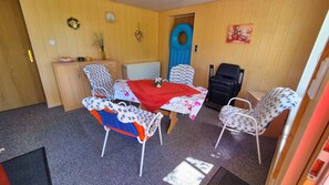 Ein Zimmer mit Esstisch, Stühlen, einer kleinen Kommode, einem Heizkörper und einer Tür.