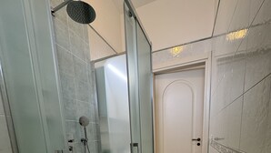 Lasiseinöillä varustettu suihku, jossa on käsisuihku ja seinään asennettu hana.