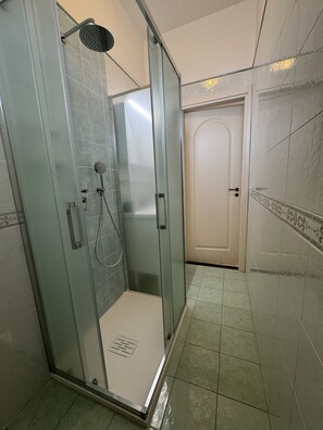 Eine Duschkabine mit Handbrause und am Wand montiertem Wasserhahn.