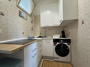 Eine kompakte Küche mit weißen Schränken, einer eingebauten Waschmaschine und einer kleinen Arbeitsfläche mit Kaffeemaschine.
