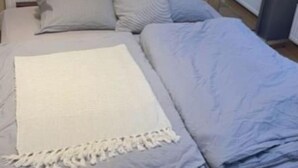 A bed with a white blanket and pillows, a radiator, and a window with curtains. - Beautiful city apartment (Würzburg)