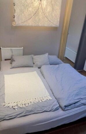 Ein Bett mit weißer Decke und Kissen, ein Heizkörper und ein Fenster mit Vorhängen.
