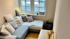 A cozy room with a grey sofa, a small table, and a window with a view of buildings. - Beautiful city apartment (Würzburg)