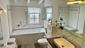A modern bathroom with a bathtub, toilet, sink, and large mirror. - Beautiful city apartment (Würzburg)