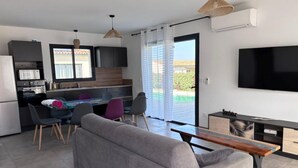 A modern living room with a sofa, dining area, kitchen, and a TV.
