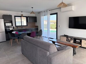 A modern living room with a sofa, dining area, kitchen, and a TV.