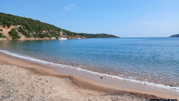 A beach with a boat, clear sky, and a hilly landscape.