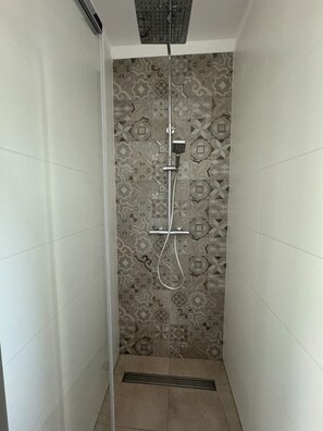 A shower with a patterned wall, a handheld showerhead, and a wall-mounted faucet.