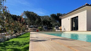 A swimming pool with a wooden deck, a modern building with large windows, and a stone wall in the background.