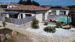 A modern villa with a swimming pool, stone walls, and a patio area.