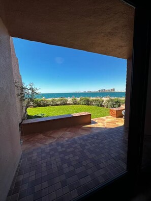Blick von einem Balkon mit Fliesenboden, einer Rasenfläche und einer entfernten Ansicht von Meer und Gebäuden.