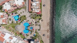 Oversigtsbillede af et kystresort med flere swimmingpools, en strand og tilstødende bygninger.