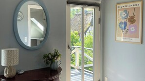 A room with a wooden ceiling, a round mirror, a table with a vase, a framed picture, and a sliding glass door leading to an outdoor deck. - Big holiday home in retreat style (Millinge)