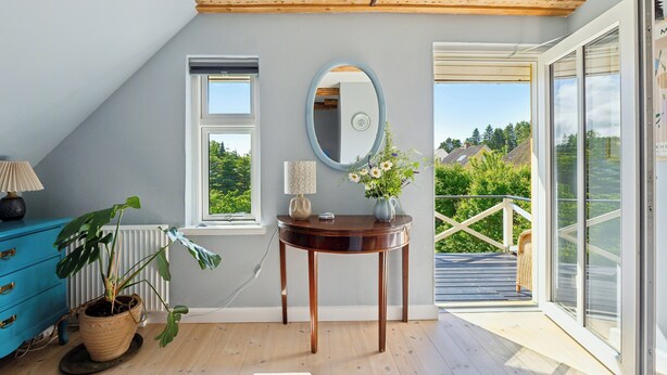 A room with a wooden ceiling, a window, a mirror, a table with a vase of flowers, a blue dresser, and a potted plant. - Big holiday home in retreat style (Millinge)