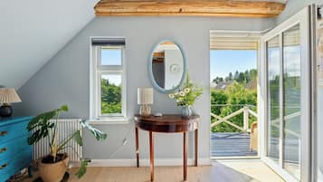 Een kamer met een houten plafond, een raam, een spiegel, een tafel met een bloevas, een blauwe dressoir en een plant in pot.