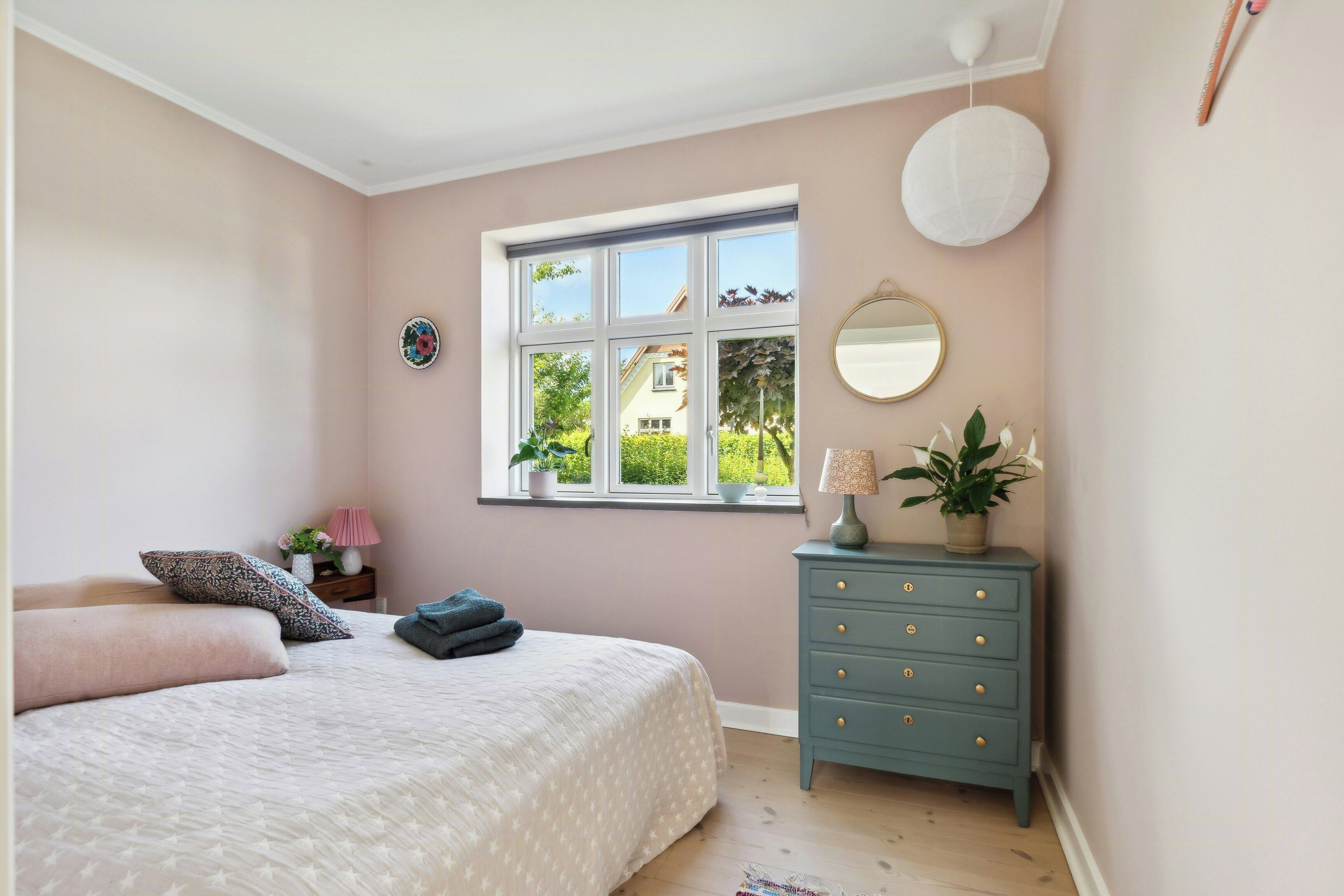 A bedroom with a bed, dresser, window, and a view of greenery outside.