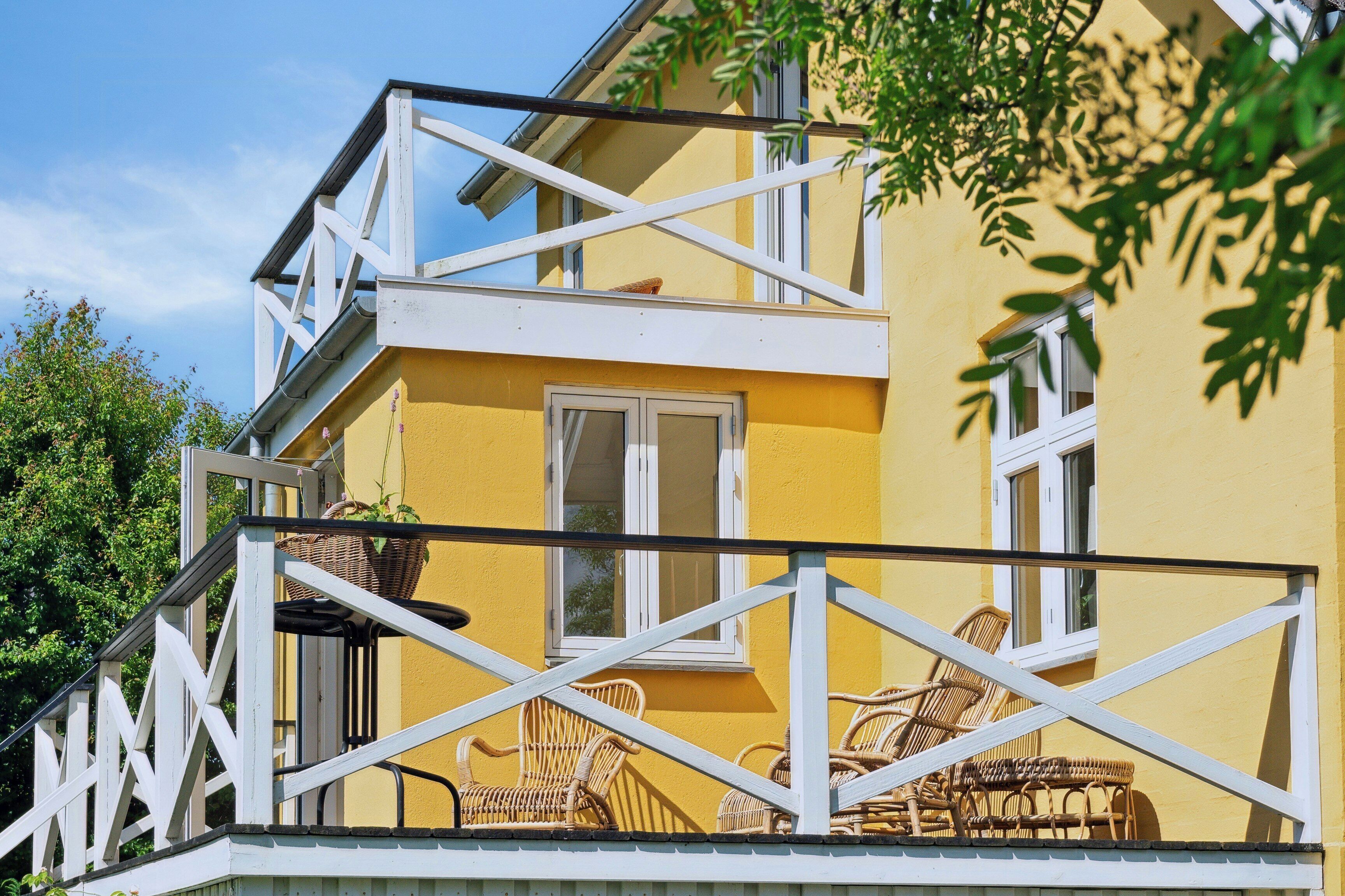 Een geel gebouw met balkon, rieten meubilair en een witte reling.
