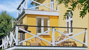 A yellow building with a balcony, wicker furniture, and a white railing. - Big holiday home in retreat style (Millinge)