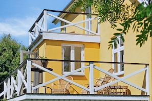 Ein gelbes Gebäude mit Balkon, Korbmöbeln und einem weißen Geländer.