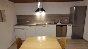 Cozinha moderna com mesa de madeira, armários brancos, eletrodomésticos de aço inoxidável e forno embutido.