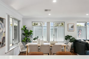 A modern dining room with a large table, chairs, and potted plants.