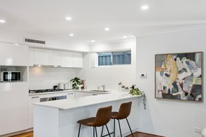 Una cocina moderna con armarios blancos, una isla central con taburetes de bar, un microondas, una estufa y una ventana sobre el fregadero.