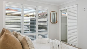Ein Schlafzimmer mit Bett, weißen Jalousien, einem Spiegel und einem begehbaren Kleiderschrank.
