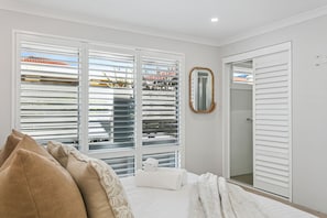 A bedroom with a bed, white blinds, a mirror, and a walk-in closet.