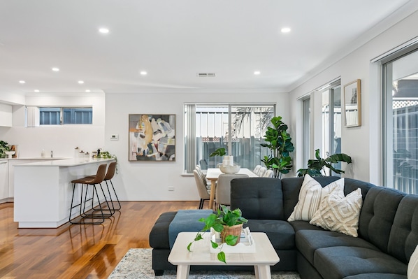 A modern living room with a sofa, coffee table, and chairs. There is a kitchen area with a bar and stools.