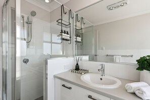 Ein modernes Badezimmer mit Duschkabine aus Glas, einem weißen Waschbecken und einem Spiegel darüber.
