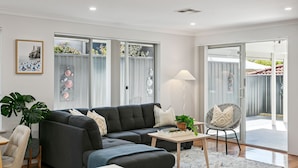 Ein modernes Wohnzimmer mit einer Eckcouch, einem kleinen Tisch, einem Sessel und einem großen Fenster mit dekorativen Glasfeldern.