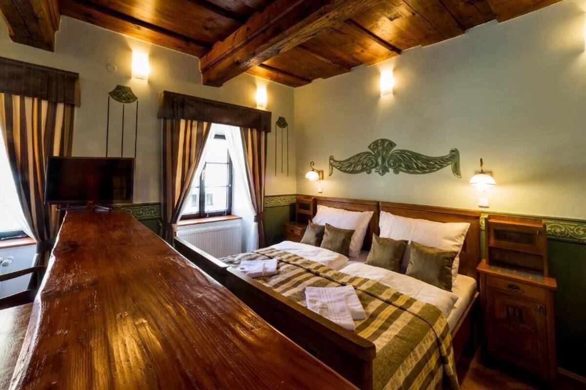 Una habitación con una cama y un banco de madera, televisión y ventana con cortinas.