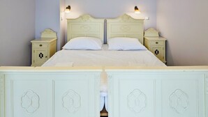A double bed with a white headboard and footboard, flanked by nightstands with lamps, in a room with herringbone-patterned wooden flooring. - Apartments Kajovska (Ceský Krumlov)