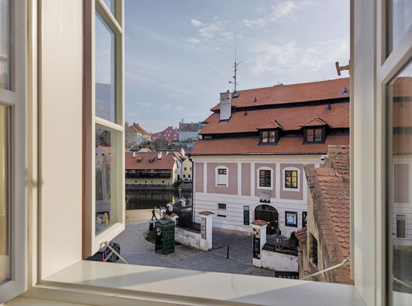 A view through a window of a building with a courtyard, featuring traditional architecture and a clear sky. - Apartments Kajovska (Ceský Krumlov)