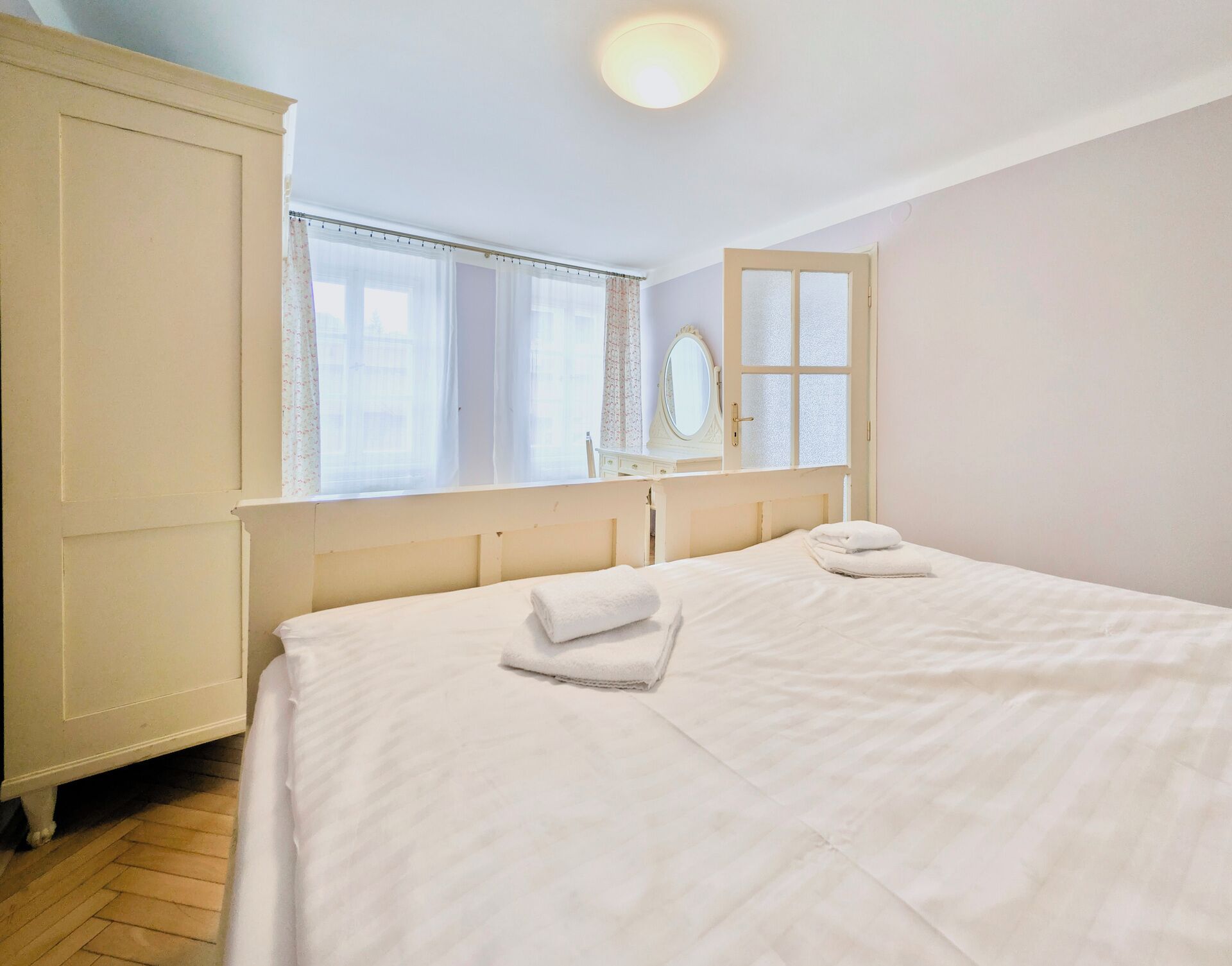 Un dormitorio con cama, armario, ventana con cortinas y espejo.