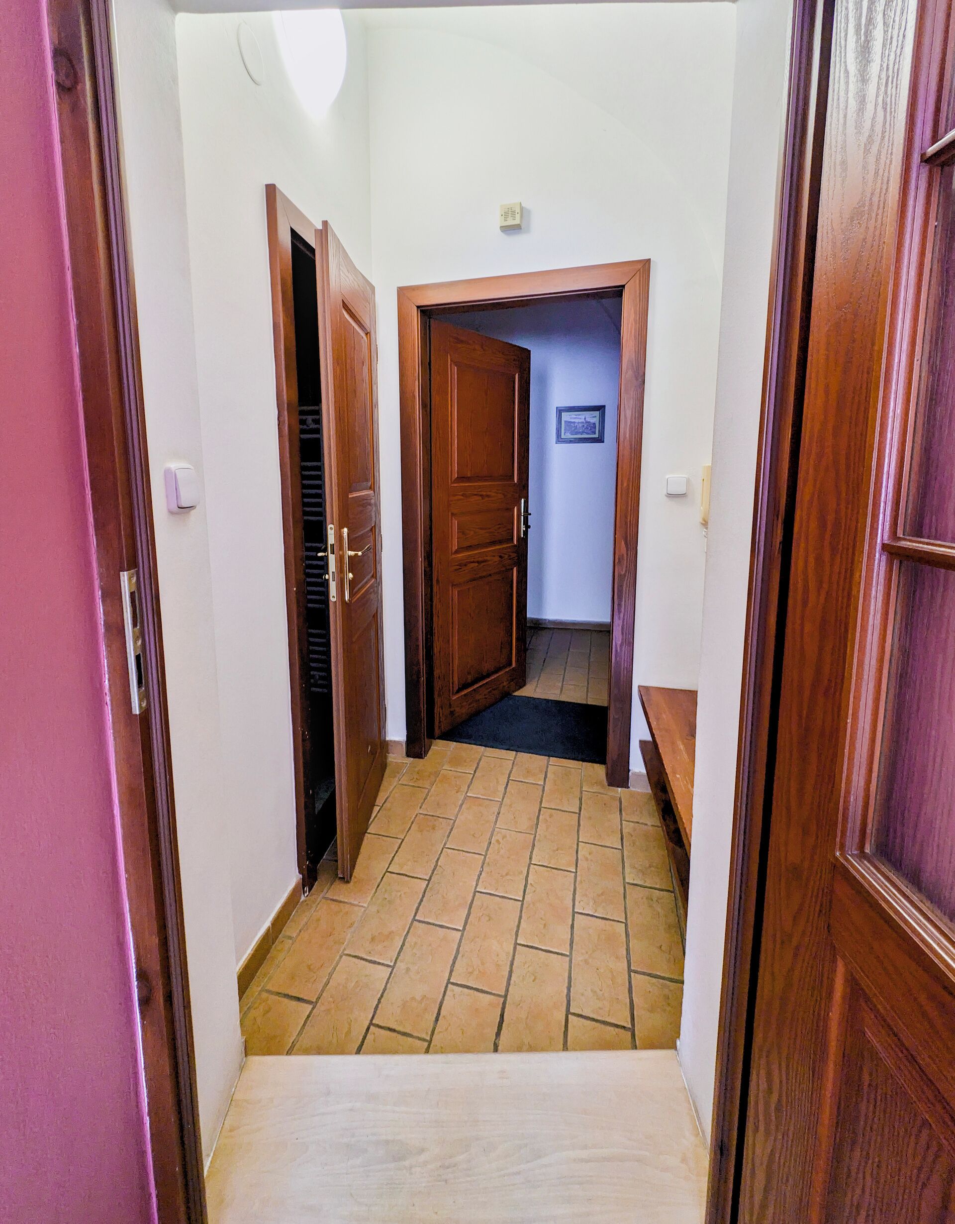 Un pasillo estrecho con puertas de madera y suelo de baldosas.