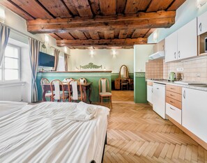 A room with a bed, wooden ceiling, a dining table with chairs, a kitchen area, and a green accent wall. - Apartments Kajovska (Ceský Krumlov)