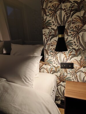 A hotel room with a bed, a nightstand, a wall-mounted lamp, and a patterned wallpaper.
