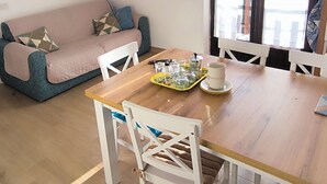 En hyggelig opholdsstue med et træbord, hvide stole, en lyserød sofa med mønstrede puder og et billede på væggen.
