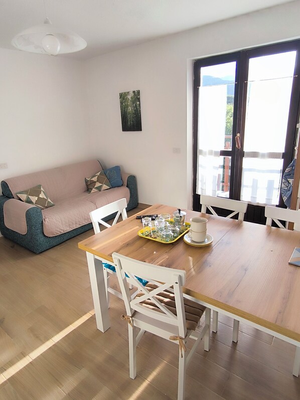Un rincón acogedor con una mesa de comedor de madera, sillas blancas, un sofá rosa con cojines estampados y un cuadro en la pared.