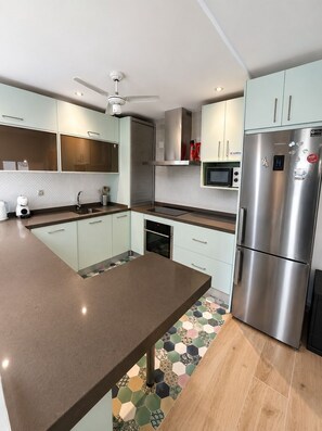 Eine moderne Küche mit einem Edelstahl-Kühlschrank, einer Mikrowelle und einem Deckenventilator.