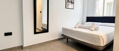 A modern bedroom with a bed, a large mirror, a picture on the wall, and a window with a view.