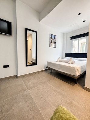 Une chambre Ă coucher moderne avec un lit, un grand miroir, un tableau au mur et une fenĂȘtre donnant sur un beau paysage.