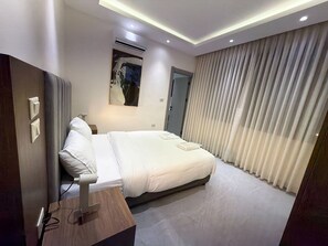 A modern hotel room with a bed, bedside table, and a painting on the wall. - 201 JRE Apartment With Stunning Boulevar (Amman)