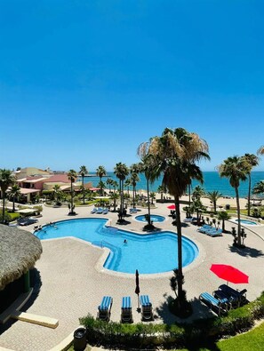 Ein Poolbereich eines Resorts mit freiem Blick auf den Ozean, Liegestühlen und Palmen.