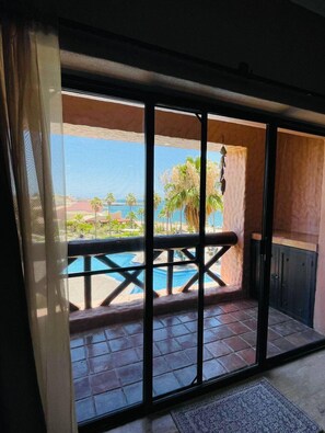 Ein Zimmer mit einer großen Schiebetür zu einem Balkon mit Pool und Palmen.