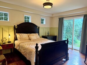 Quarto com cama grande, mesas de cabeceira, luminária e vista para o verde pela janela.