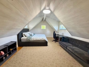 Een slaapkamer in een loft met een schuine wand, een bed, een bureau, een bank en een boekenkast.