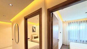 Una camera d'albergo con un letto, un comodino, uno specchio e una porta che dà su un'altra stanza.