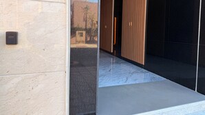 Ingresso di un edificio moderno con una parete strutturata, una porta in metallo e un pannello di vetro che riflette il cielo.